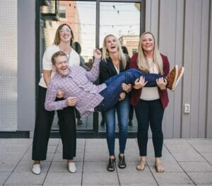 team holding ben three social assurance employees holding another employee and laughing