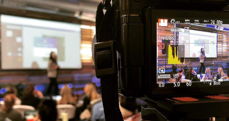 A camera recording a presenter on a stage