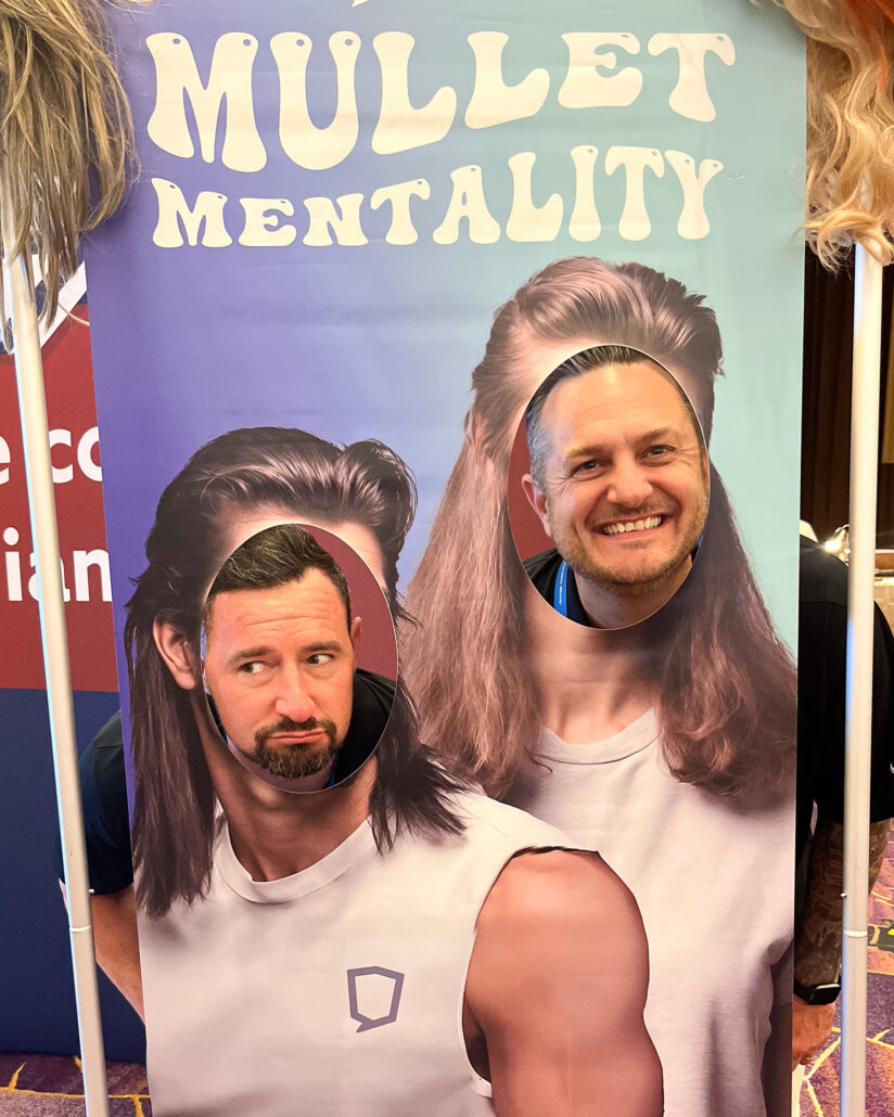Two attendees pose in the #MulletMentality photo cutout.