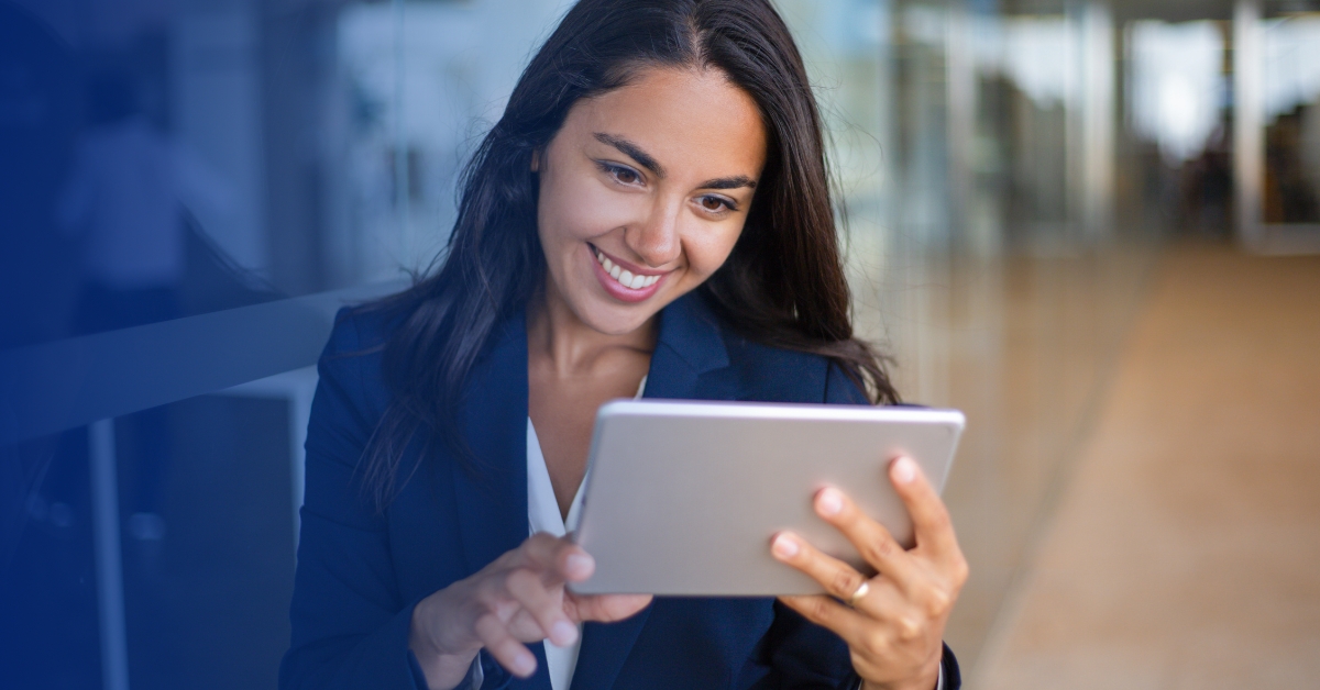 Smiling professional woman in a blazer using a tablet in a bright, modern office setting.