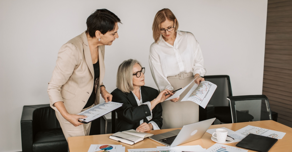 Three professionals in business attire gathered around a desk, discussing documents.